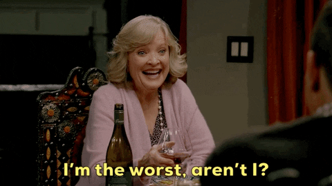 An older woman holding a glass fo wine saying, "I'm the worst, aren't I?"