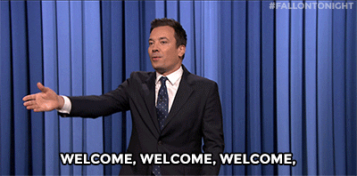 A white man gesturing across the room and saying, "Welcome" repeatedly.