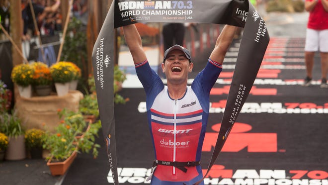 Photo: An IRONMAN 70.3 participant lifting the finish line banner above his head.