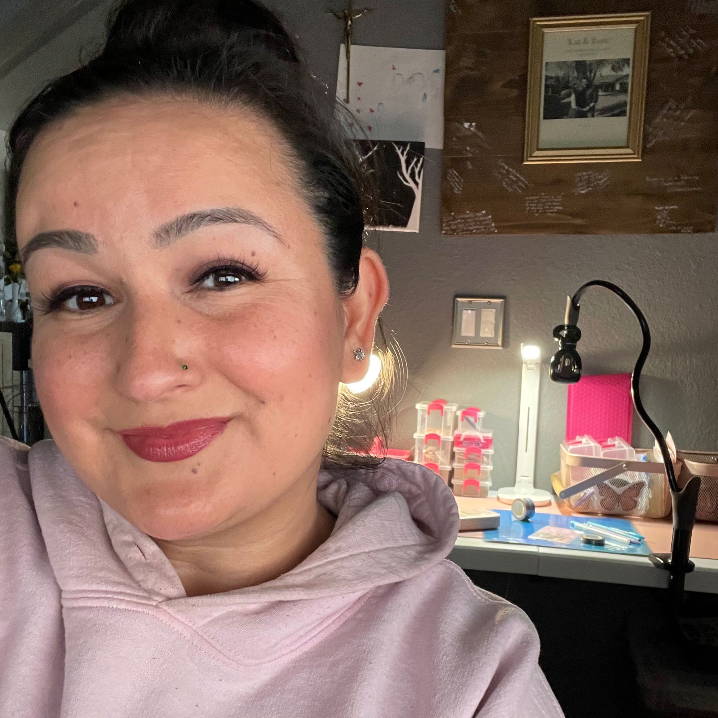 Photo: A woman smiling at the camera, sitting in front of a desk with sticker-making equipment.
